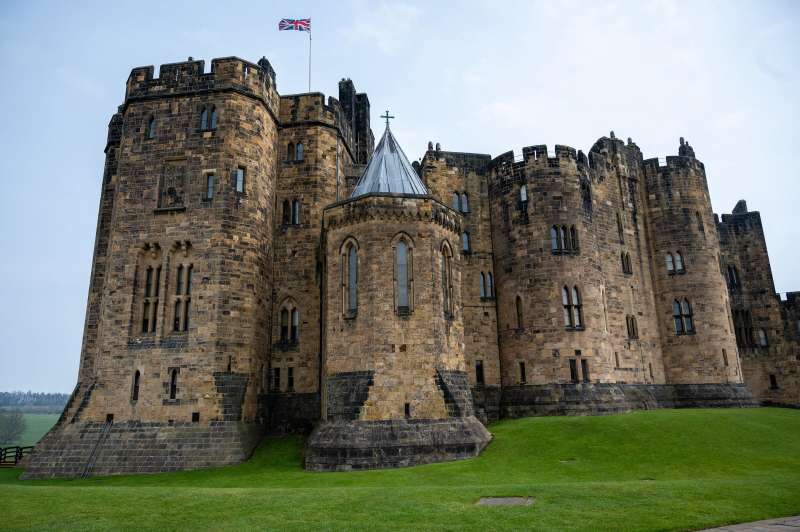 A large yellow stone building rises out of a lush green landscape, with a Union Jack flying above it.