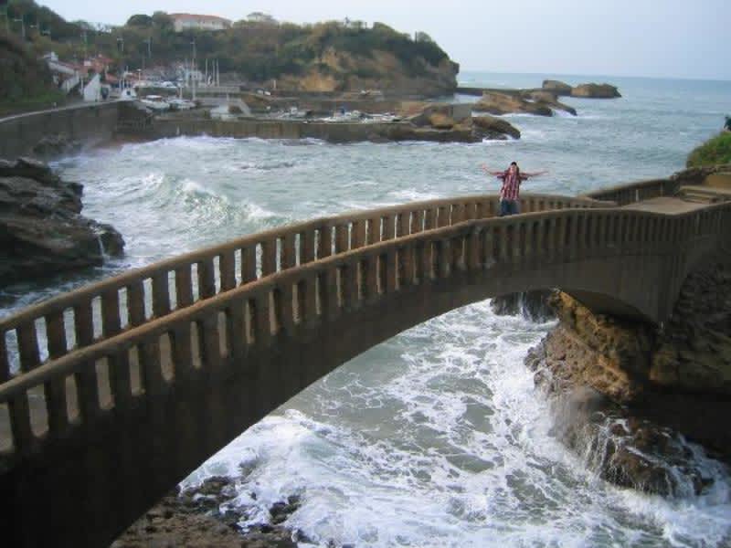 A person standing on a bridge overlooking the vast ocean, surrounded by serene blue waters.