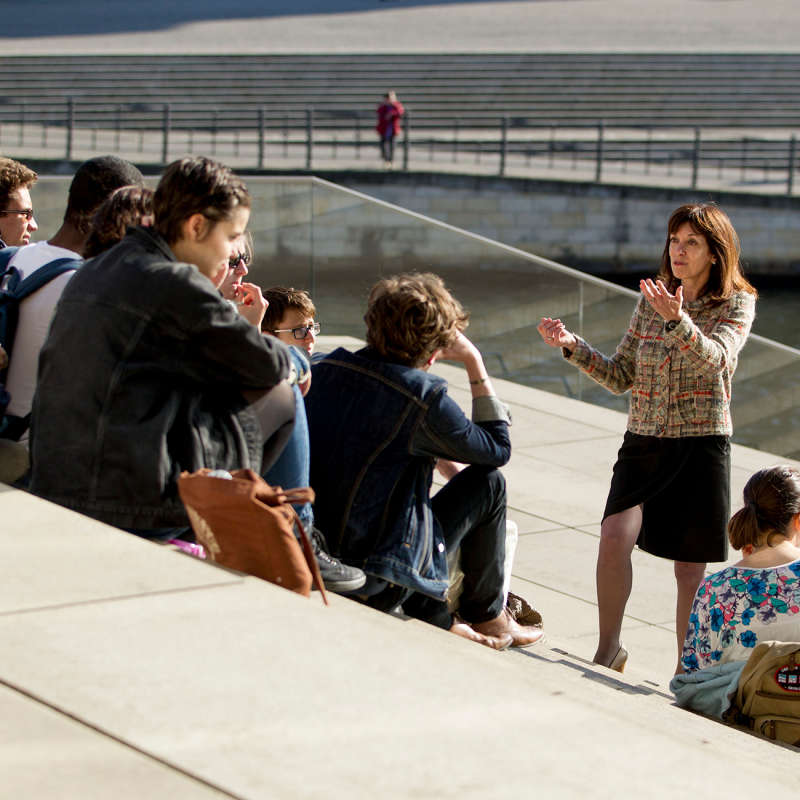 A professor lectures her class outdoors on concrete steps.