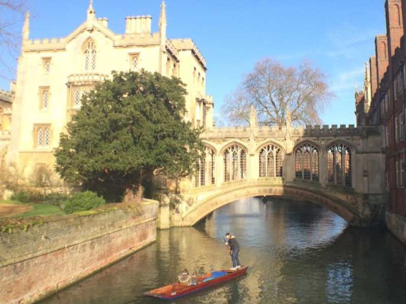 A punter guides a boat beneath the Bridge of Sighs on the River Cam in Cambridge, England on a sunny day.