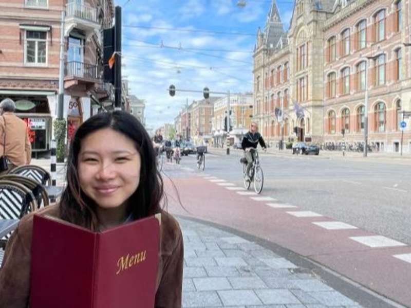 A student holding a menu sits on an outdoor table in Amsterdam.