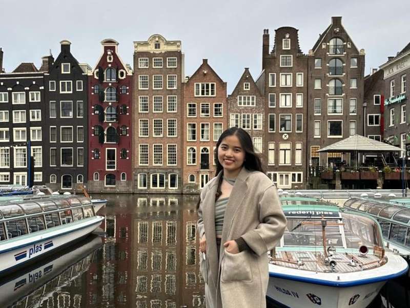 A student in front of popular row of houses and a canal in Amsterdam.