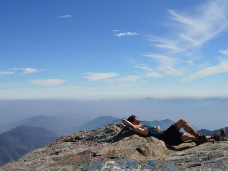 a student laying on a mountaintop in the Andes, surrounded by other mountains in the distance