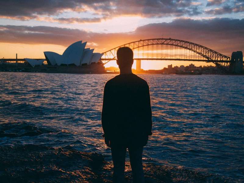 a student looking at the Sydney Bridge and Opera House at sunset