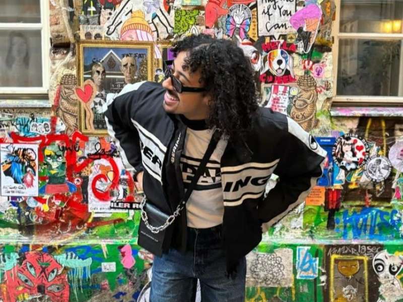 A student poses in front of a colorful sticker and graffiti-covered wall in Berlin, Germany.