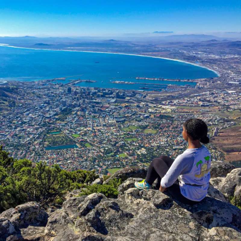 A student sitting on a mountaintop overlooking Cape Town.