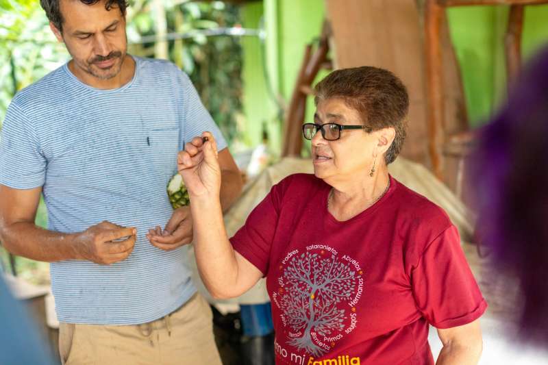 A woman holds up a single coffee bean, speaking to an audience out of view.