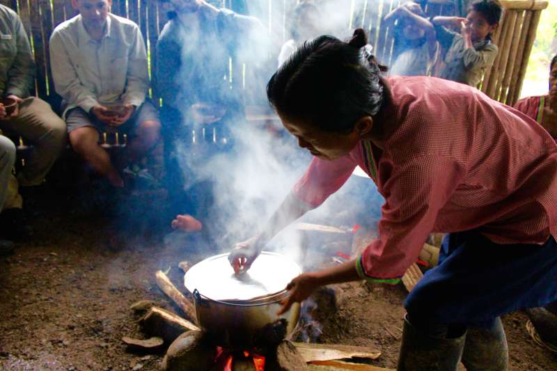 A woman leans over a steaming pot cooking on a woodfire. 