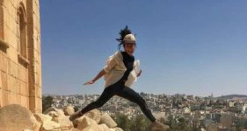 A woman leaping on rocks with a city skyline in the background.