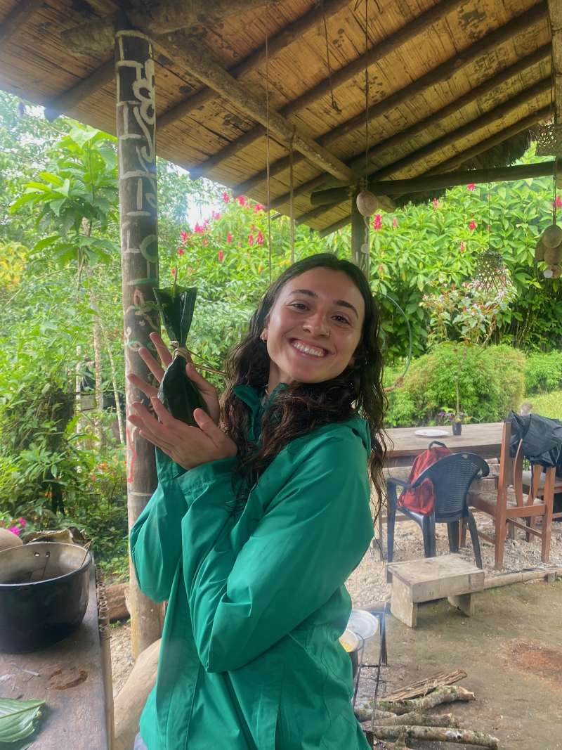 A woman smiles for the camera as she holds food wrapped in leaves.