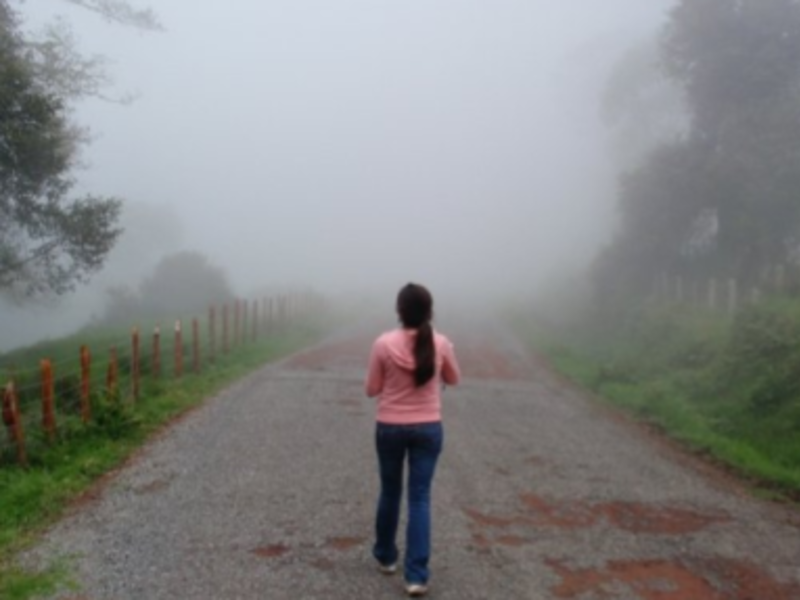 A woman walking down a foggy road, surrounded by mist and uncertainty.