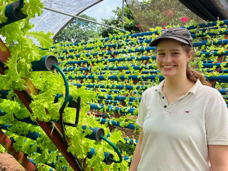 An intern smiles amidst rows of hydroponic farmed lettuce.