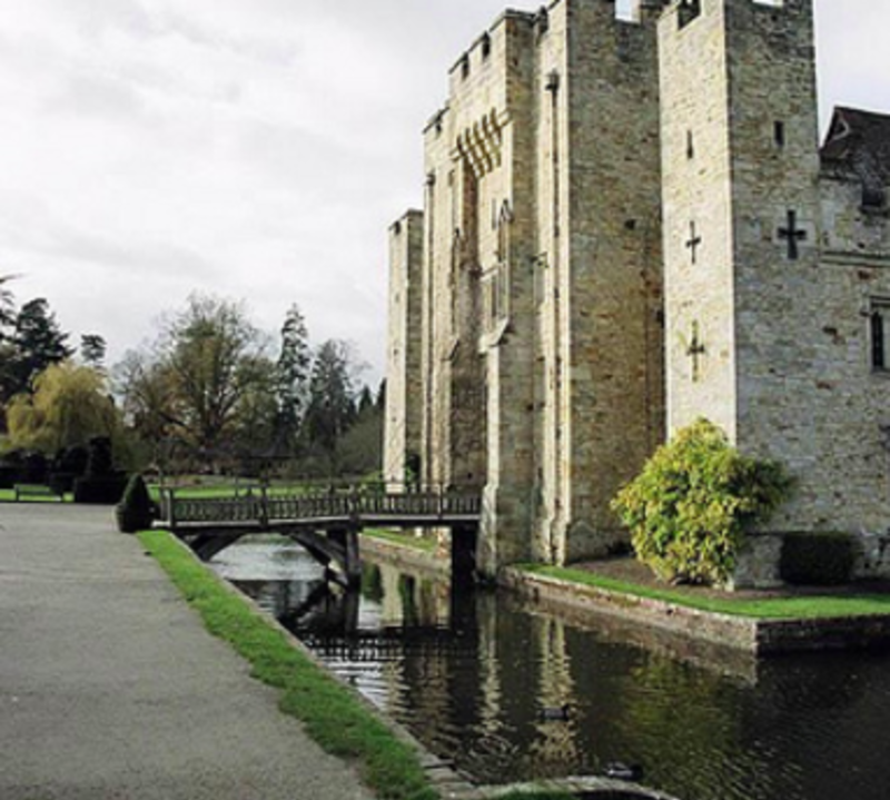 Castle with bridge over river, surrounded by lush greenery.