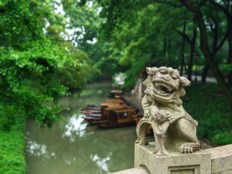 Chinese stone bridge statue with river and boats in the background