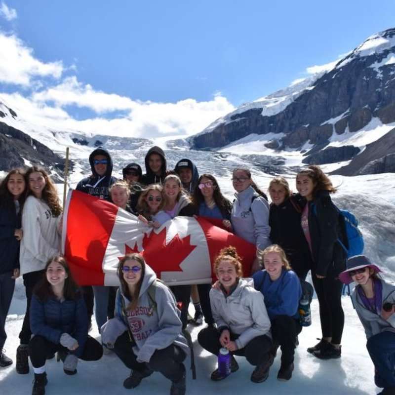 group of teens pose with the Canadian flag on a summer travel tour