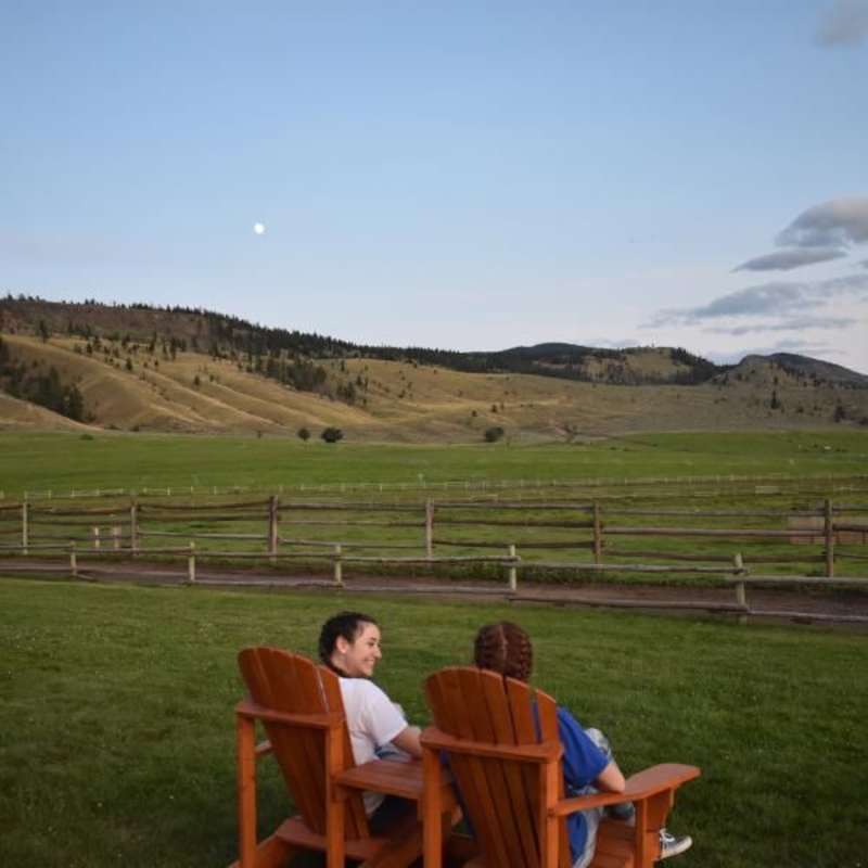 two teens sit in chairs on a canadian ranch at sunset