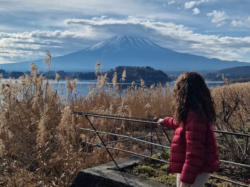EF student in a red jacket admiring Mount Fuji across a lake on a clear day in Japan.