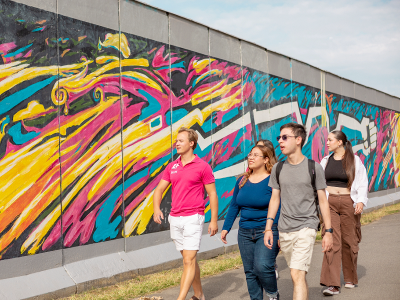 EF students walking past colorful street art on the Berlin Wall, exploring the city during a cultural activity.