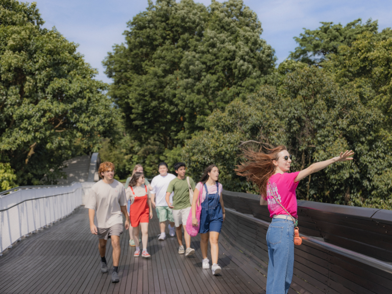 EF students walking with a staff leader across Henderson Waves bridge in Singapore, surrounded by lush greenery.