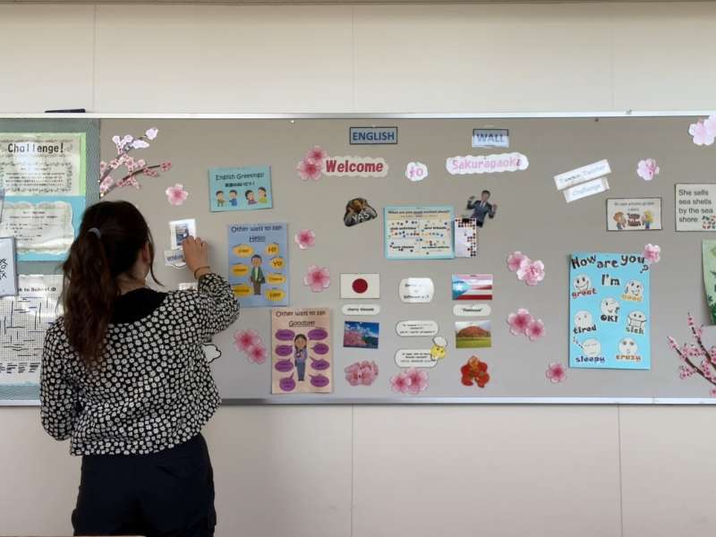 Female teacher rearranges resources on classroom display board.