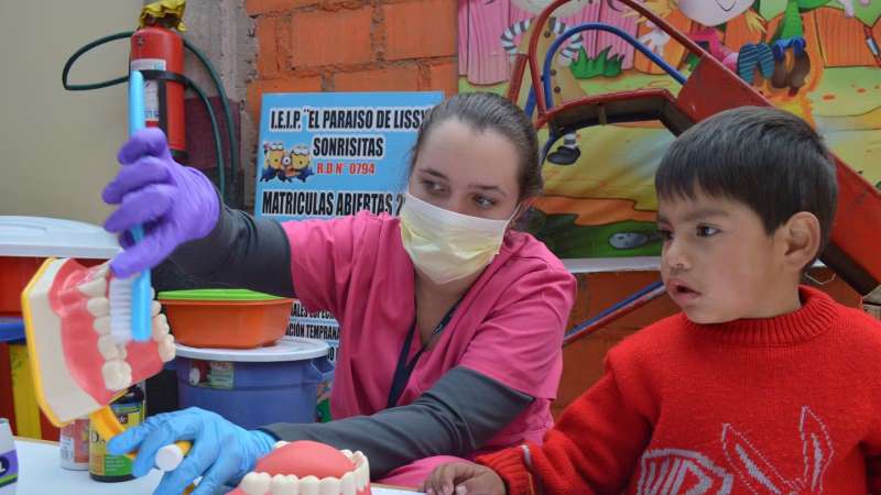 Female Volunteer Demonstrating how to Brush Teeth to a Child