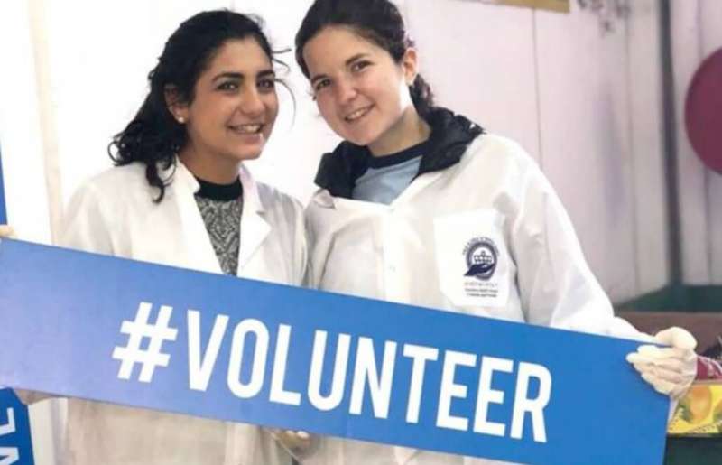 two girls holding a hashtag volunteer sign