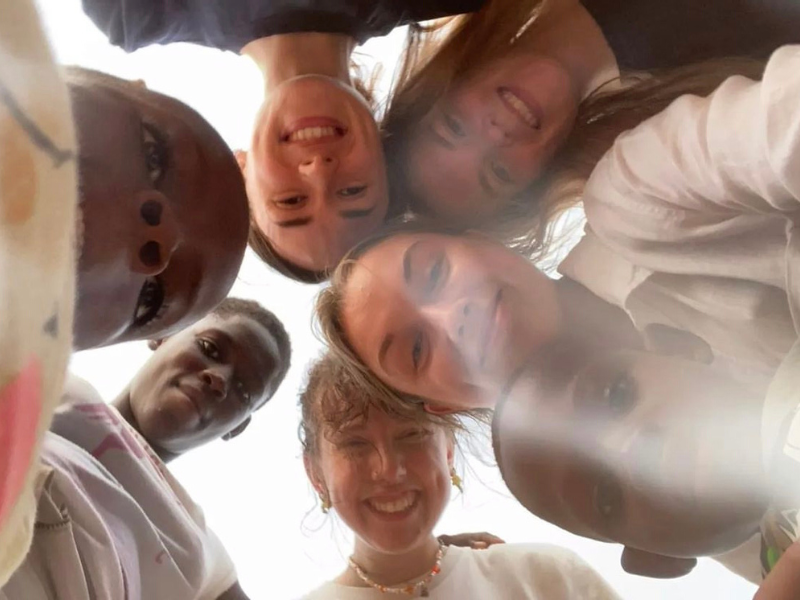 Four volunteers take a selfie with three children from below, so they are all looking down on to the camera.