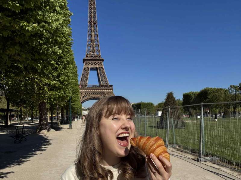 Girl eating crosissant beside Eiffel Tower