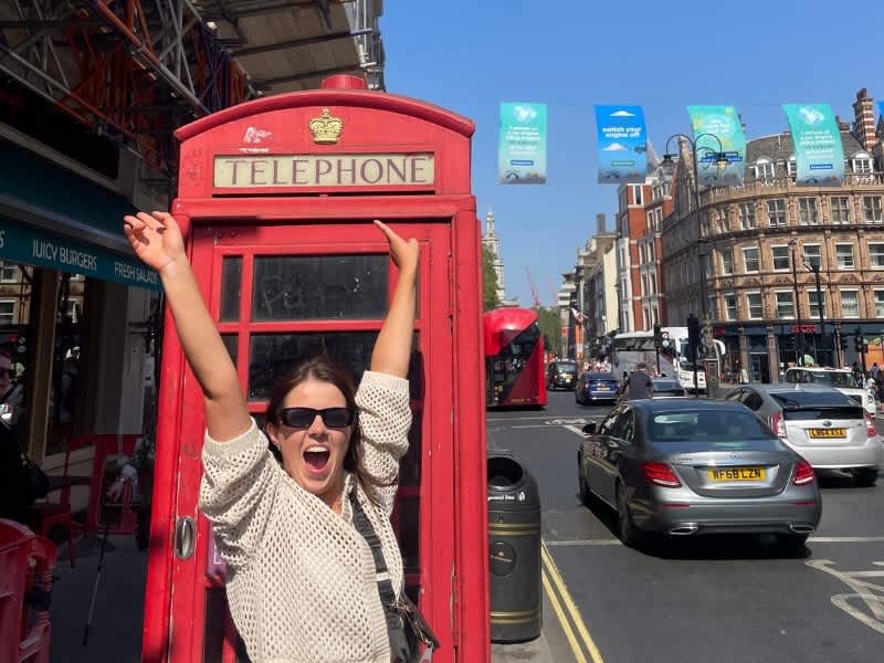 Girl standing in front of a British red telephone box