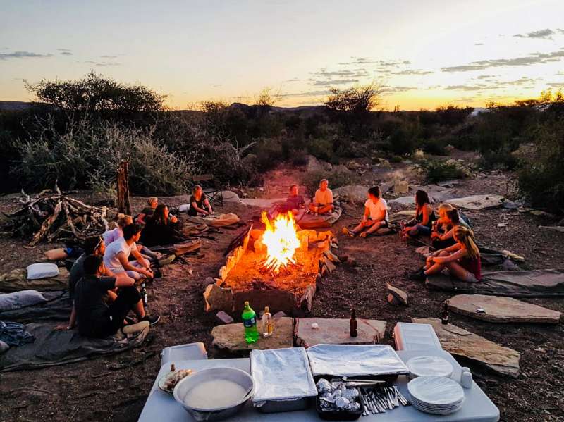 Group of ACE volunteers relaxing around the campfire in the late afternoon
