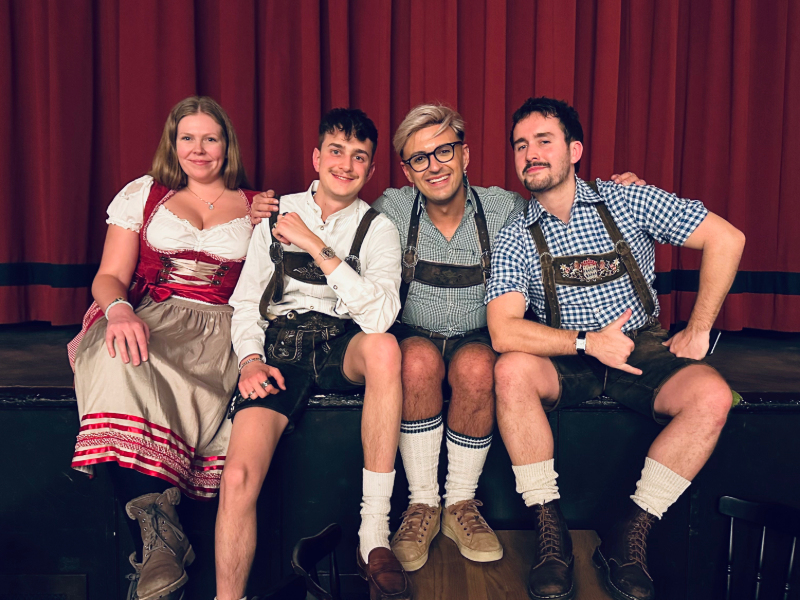 Group of EF Gap Year students dressed in traditional Bavarian lederhosen and dirndl, sitting together in Munich, Germany, and experiencing local culture.