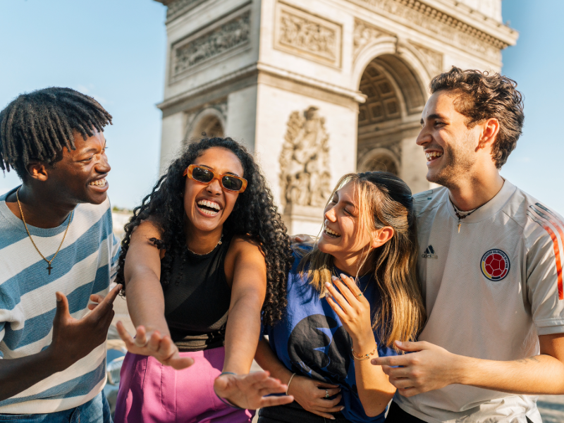 Group of EF students laughing together in front of the Arc de Triomphe in Paris on a sunny day.