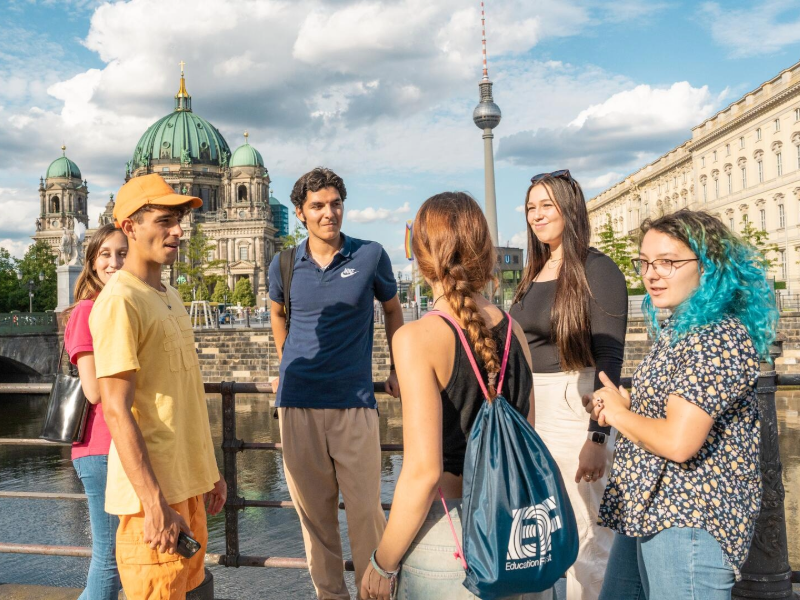 Group of EF students talking by the river in Berlin, with the Berlin Cathedral and TV Tower in the background.
