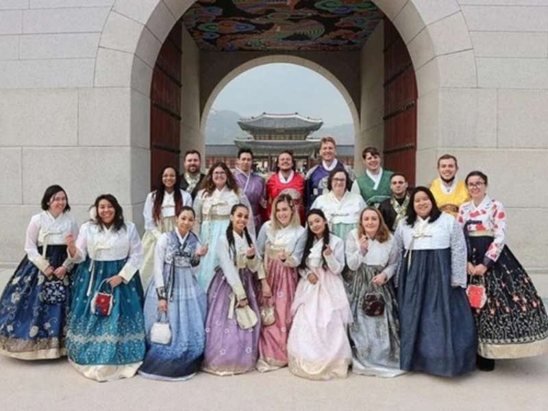 International teachers and students wearing traditional hanbok at a historic palace in South Korea.