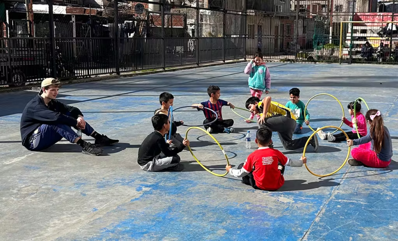 IVHQ Volunteer teaching a class of kids a game involving hula hoops