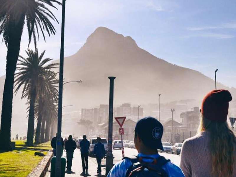 People walk near the ocean with a view of a mountain in front of them in Cape Town