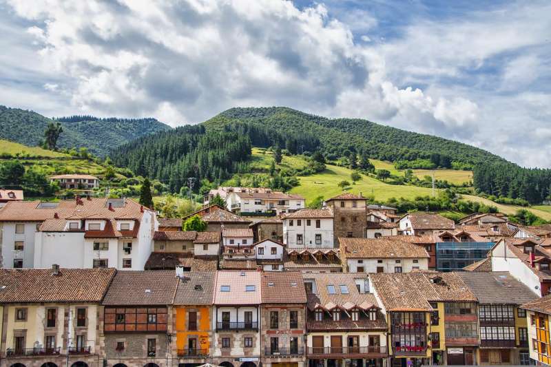 Quaint Spanish town with tiled rooftops and lush green hills behind.