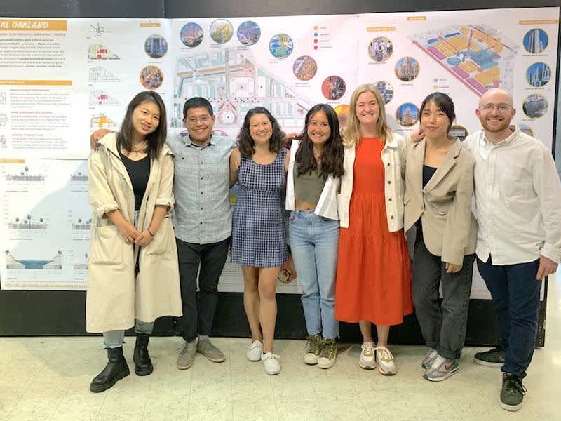 Seven students posing in front of plans pinned to the wall