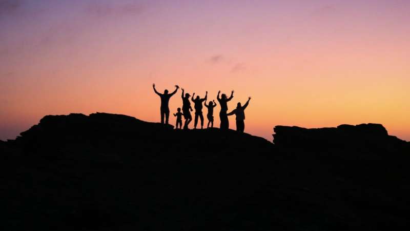 Silhouettes of people with arms raised against a sunset.
