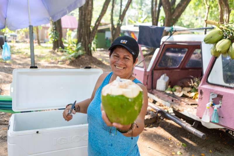Smiling woman holds out fresh coconut 