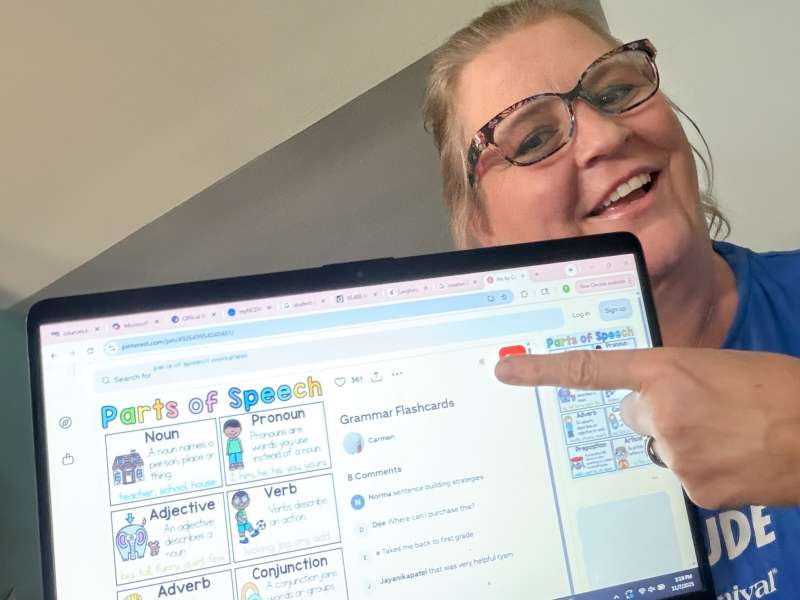 Smiling woman pointing to laptop screen, which shows teaching resources.
