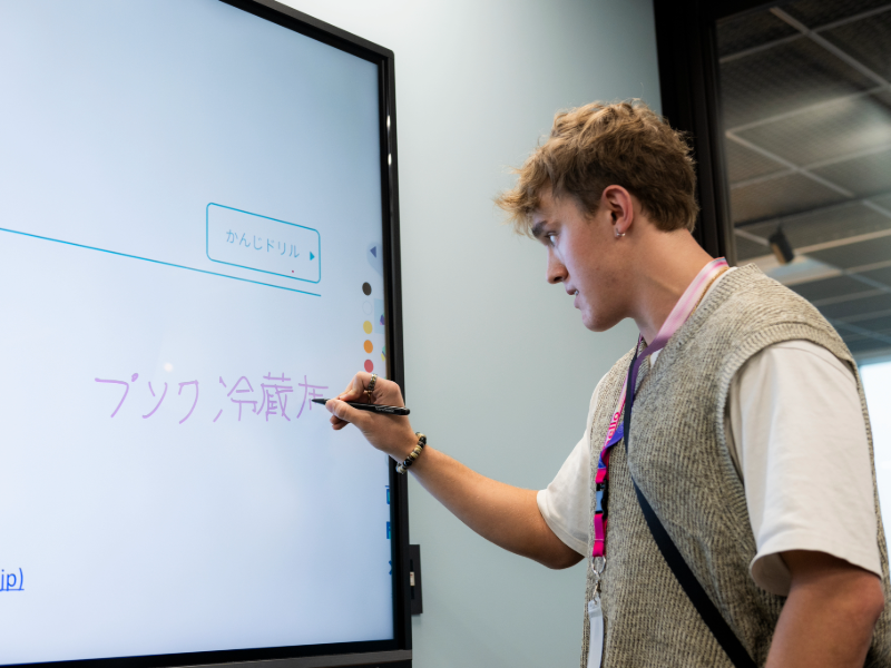 Student practicing Japanese writing on an interactive digital whiteboard during class.