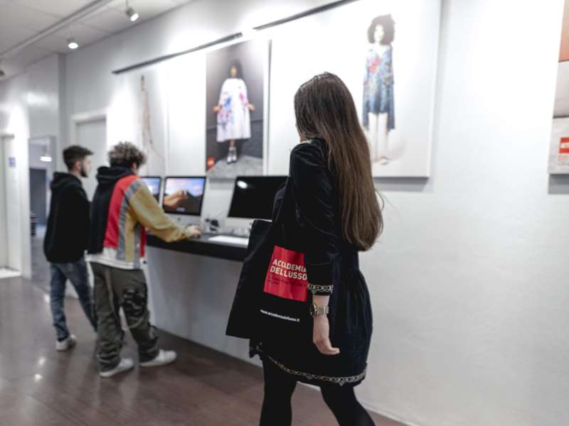 Student walking down a corridor with art on the walls. Two other students are standing at computers