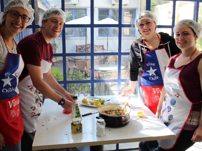 students gathered around a table in aprons cooking Chilean food