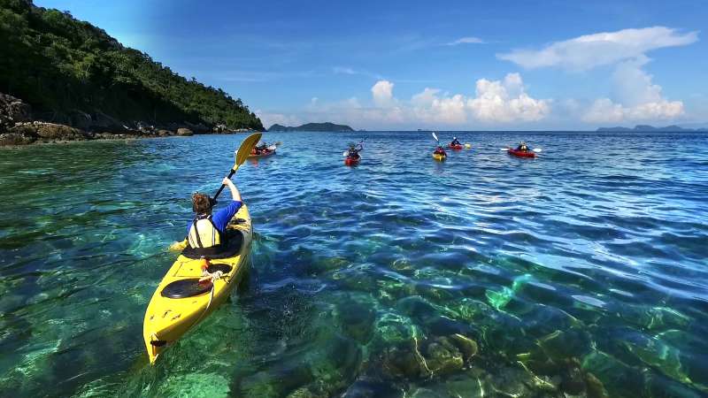 Students ocean kayak through clear blue water with an island in the background