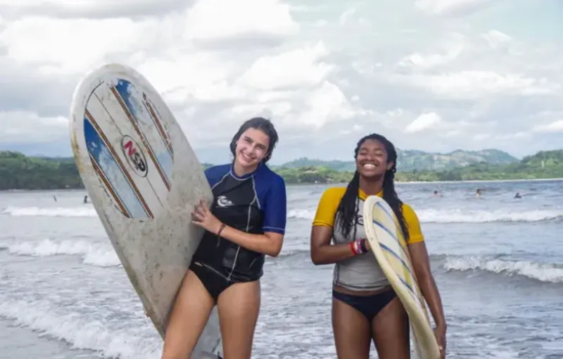 Students on beach holding surfboards
