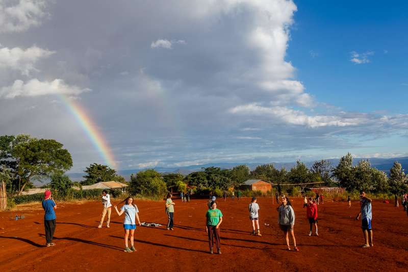 Students on red soil with a rainbow in the background in Tanzania
