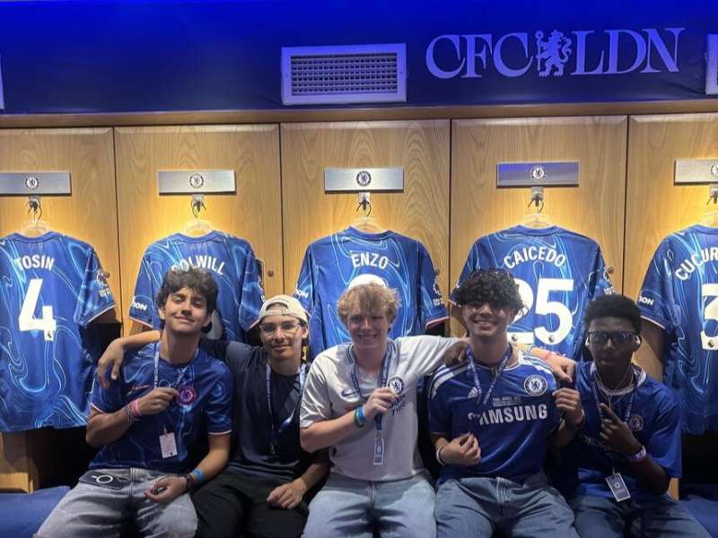 Students posing in locker room in front of jerseys at Chelsea Stadium