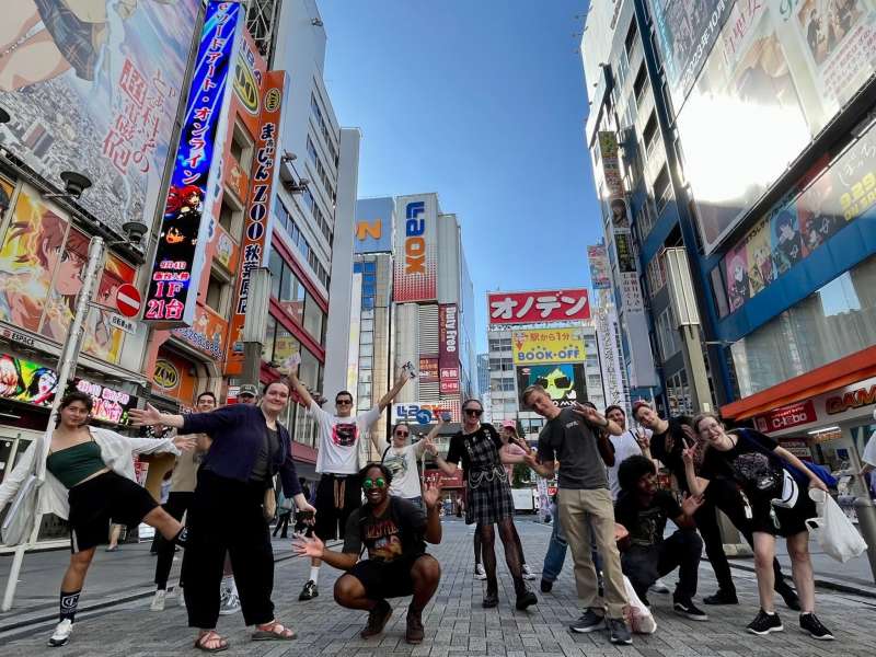 Students posing in the vibrant Akihabara neighborhood with brightly colored signs on tall buildings