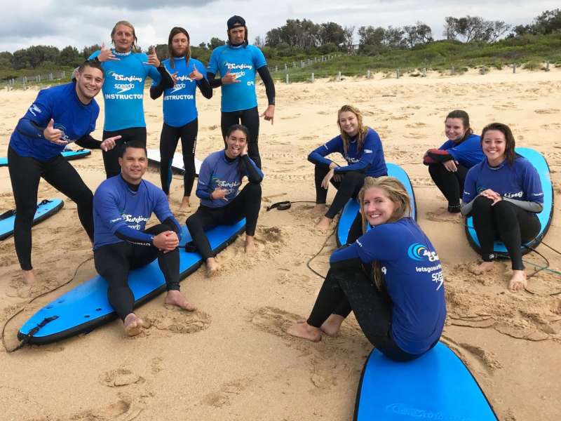 students sitting on surf boards on the beach during surf lessons